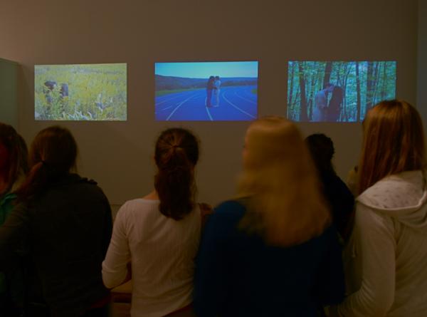 Gallery visitors viewing a 3 channel video piece by Bang Geul Han
